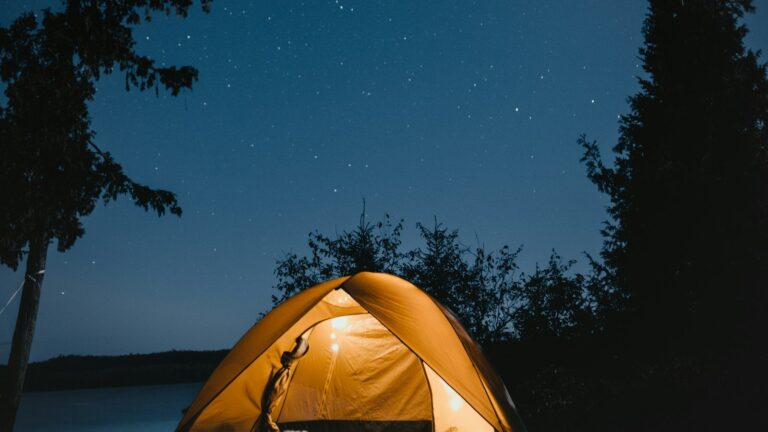 Lit tent at a lakeside campsite under a starry sky